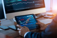 businessman-checking-stock-market-on-digital-tablet-and-a-desktop-computer-with-stock-exchange-graph-on-screen-financial-stock-market-analyzing-data-in-office-background-2